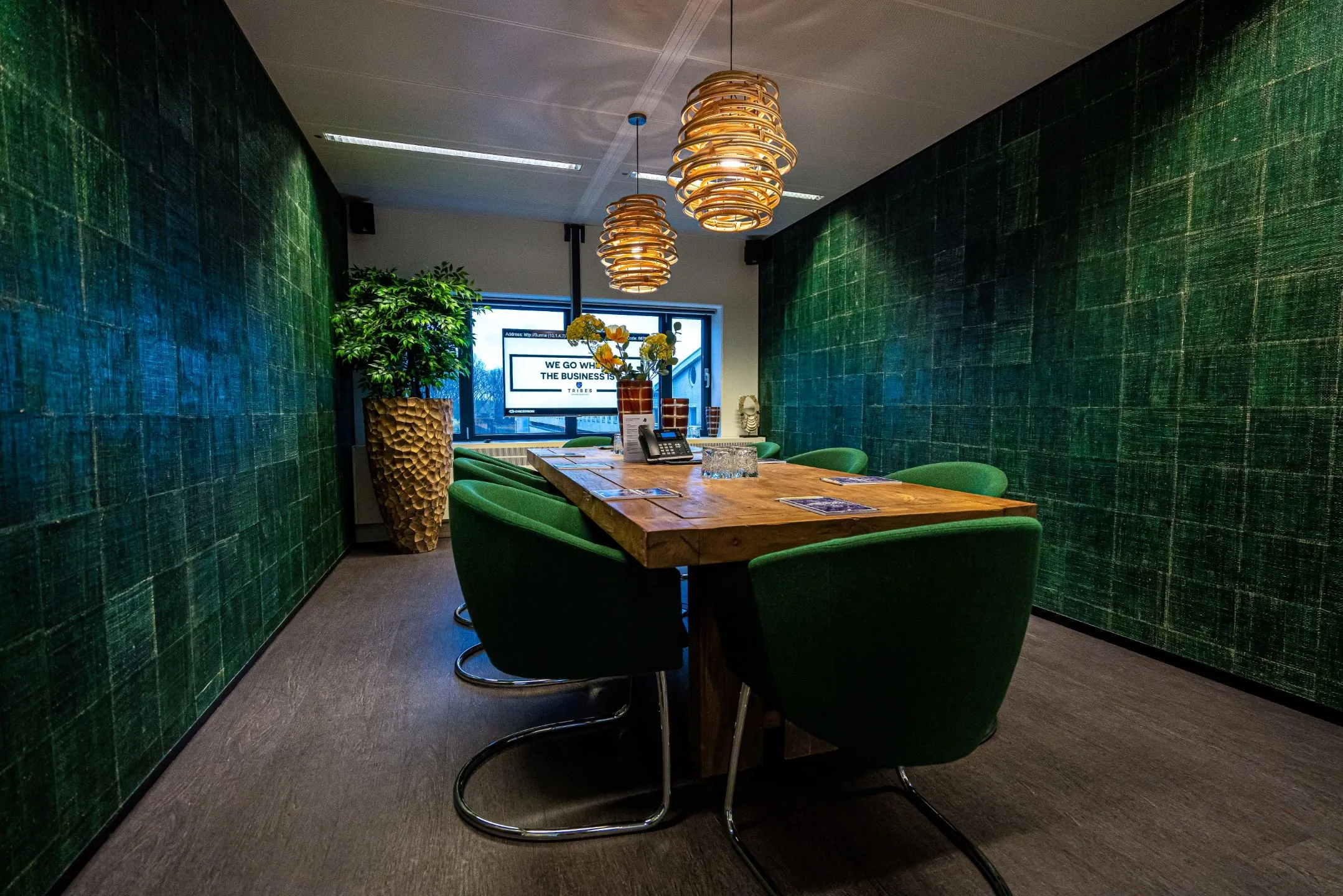 Moderne vergaderruimte op de Zuidas in Amsterdam met groene stoelen, houten tafel en sfeervolle verlichting.