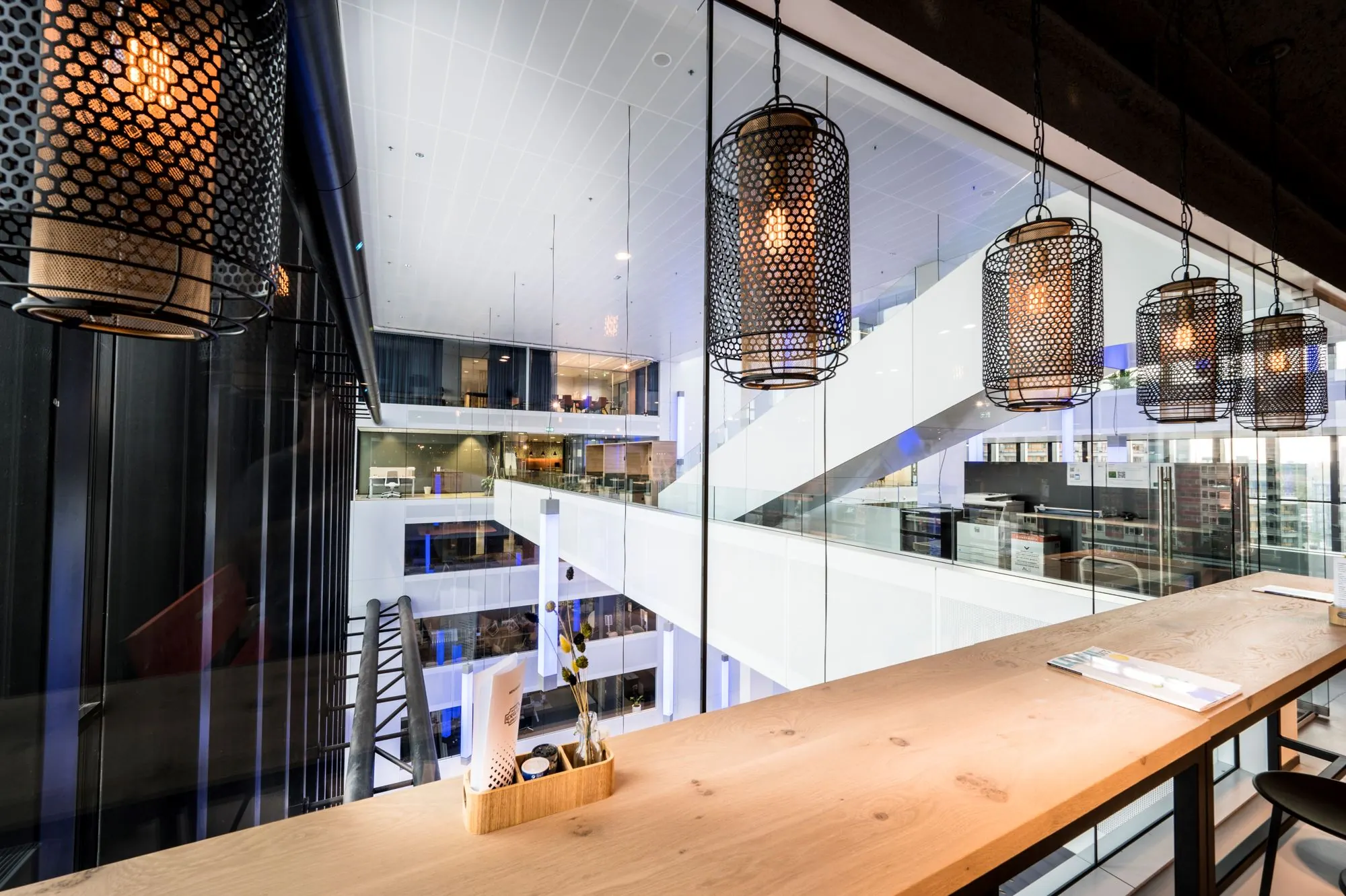 Moderne kantoorruimte met houten werkblad, hanglampen en uitzicht op het atrium van Bargelaan 200 in Leiden.