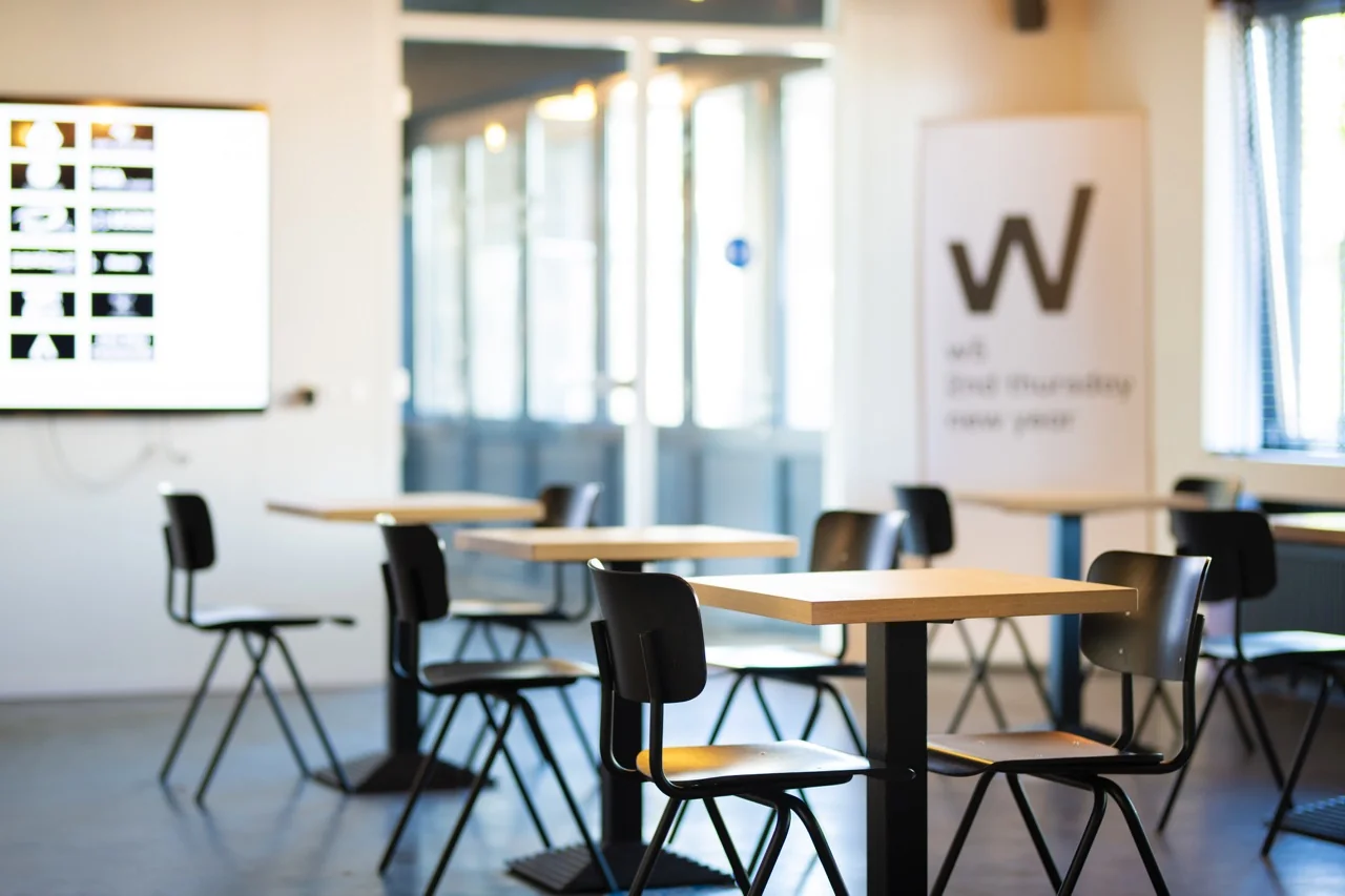 Moderne, lichte kantoorruimte aan de Brugstraat 11 in Almelo met tafels, stoelen en een presentatiescherm.