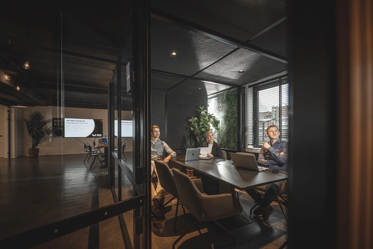 Drie mensen in een moderne vergaderruimte aan de Brugstraat 11 in Almelo tijdens een presentatie.