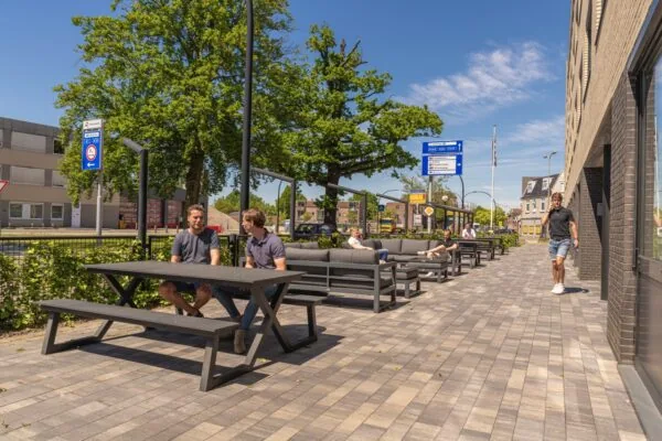 Terras met zitgelegenheid naast kantoorruimte aan de Brugstraat 11 in Almelo, waar mensen ontspannen in de zon.