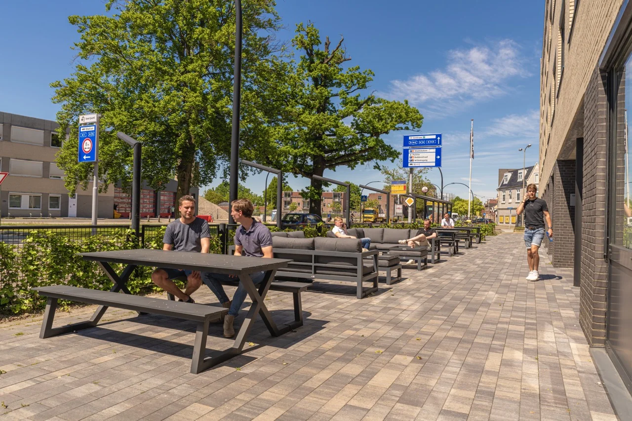 Terras met zitgelegenheid naast kantoorruimte aan de Brugstraat 11 in Almelo, waar mensen ontspannen in de zon.