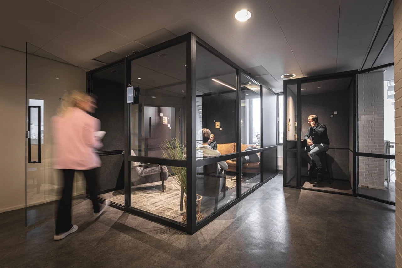 Moderne kantoorruimte met glazen vergaderruimtes en mensen in gesprek aan de Brugstraat 11 in Almelo.