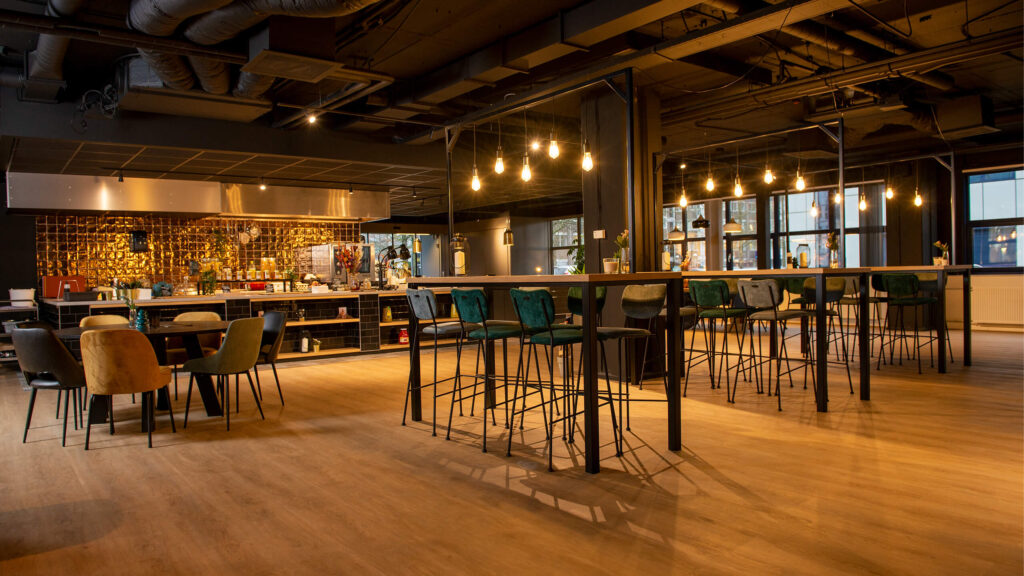 Moderne gemeenschappelijke kantoorruimte aan de Bruistensingel 400 in Den Bosch met hoge tafels, barzitjes en warme sfeerverlichting.