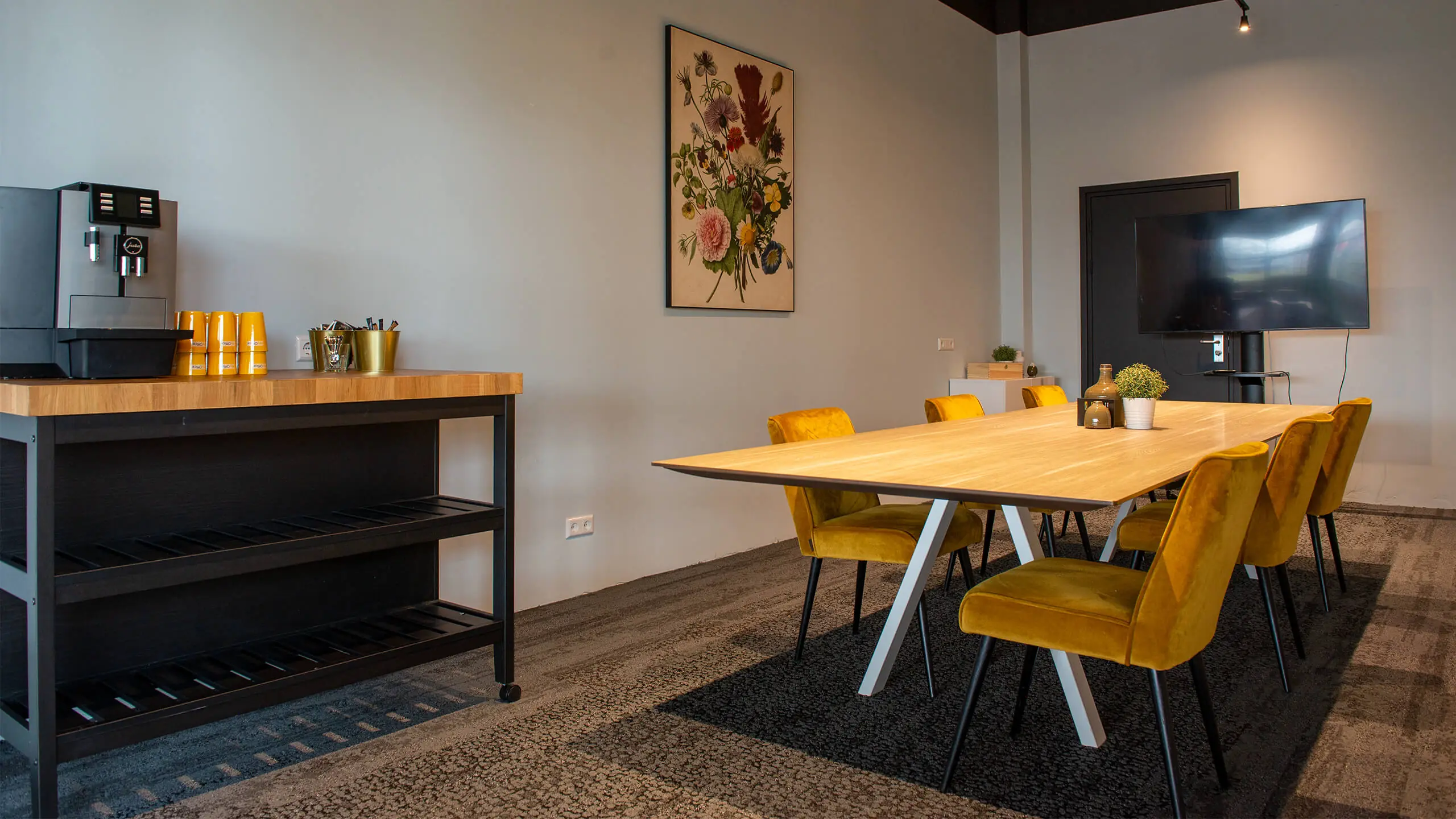 Moderne vergaderruimte aan de Bruistensingel 400 in Den Bosch met gele stoelen, houten tafel, koffiemeubel en flatscreen.