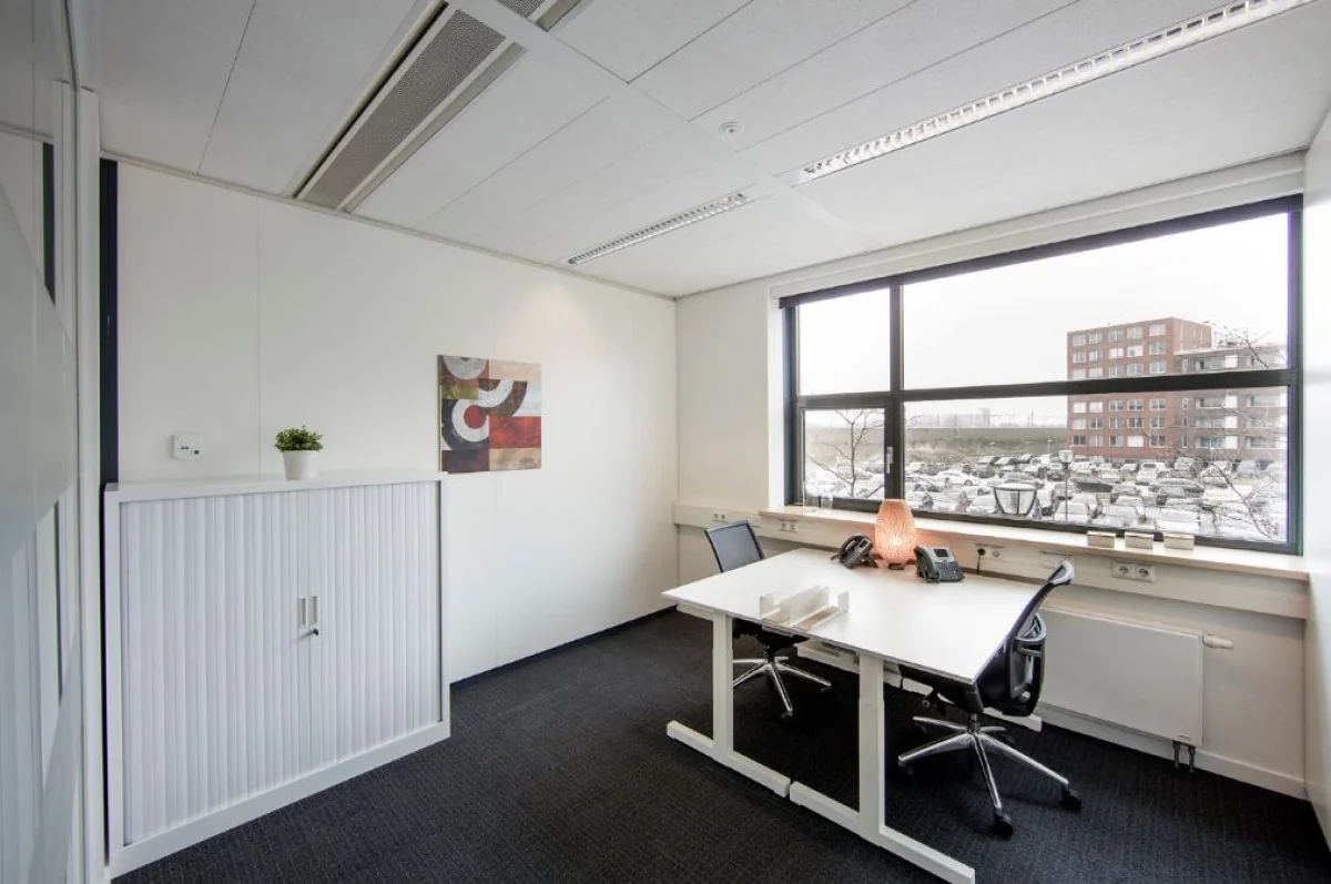 Moderne kantoorruimte aan de Ceresstraat 1 in Breda met bureau, stoelen, opbergkast en groot raam met uitzicht op parkeerterrein.