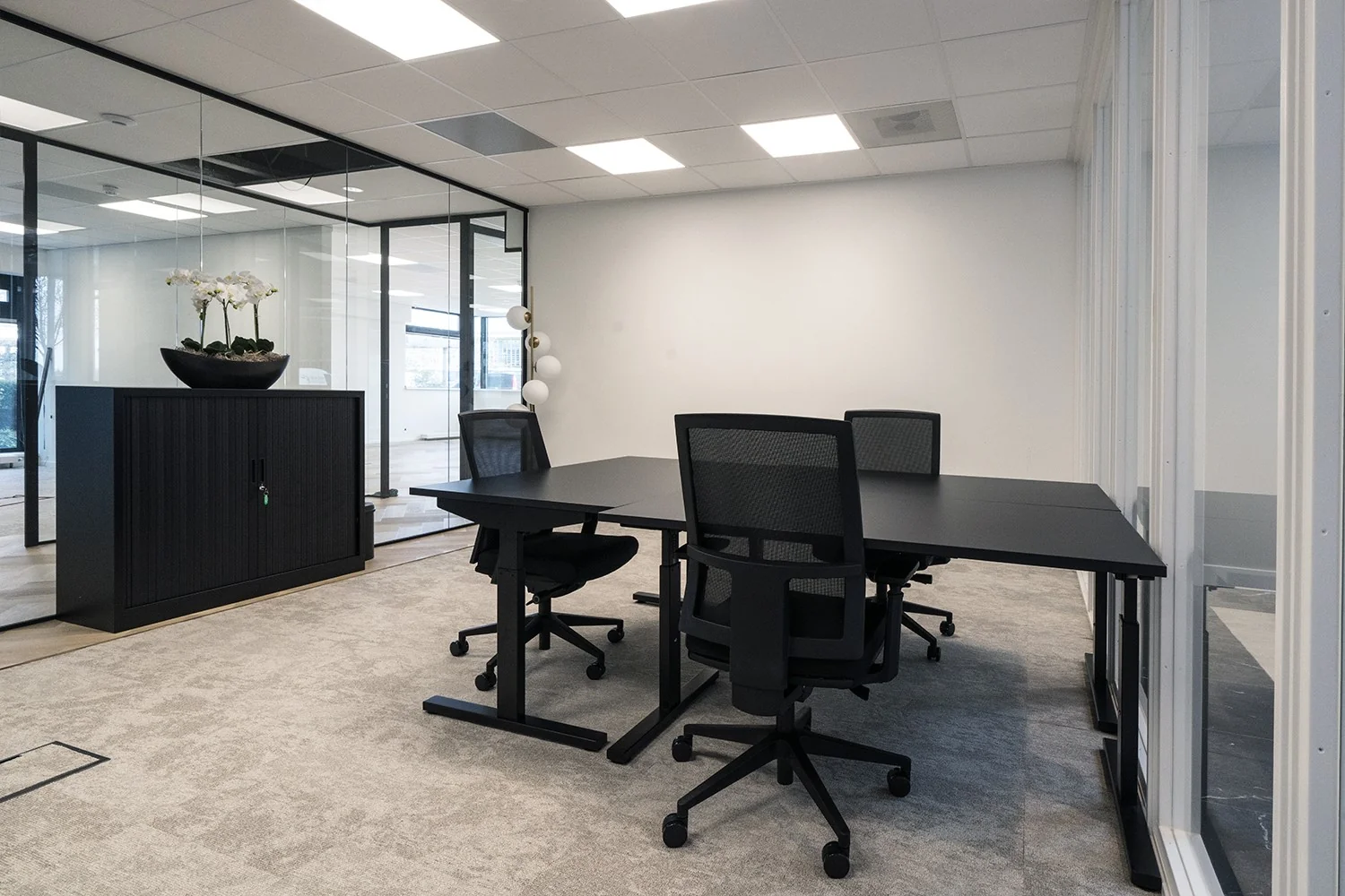 Moderne, lichte kantoorruimte in Hoofddorp met zwarte bureaus, bureaustoelen en glazen wanden.