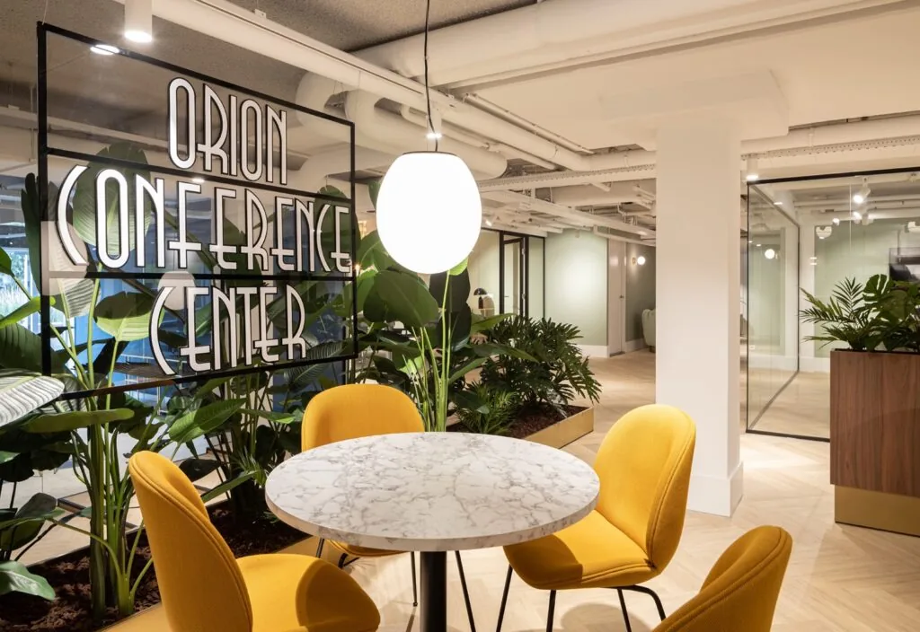 Moderne vergaderruimte in het Orion Conference Center in Hoofddorp met marmeren tafel, gele stoelen en groene planten.