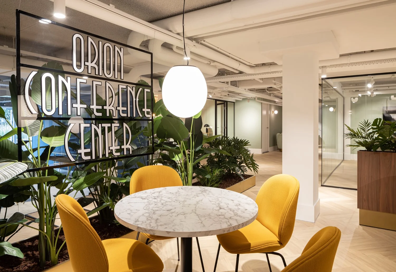 Moderne vergaderruimte in het Orion Conference Center in Hoofddorp met marmeren tafel, gele stoelen en groene planten.