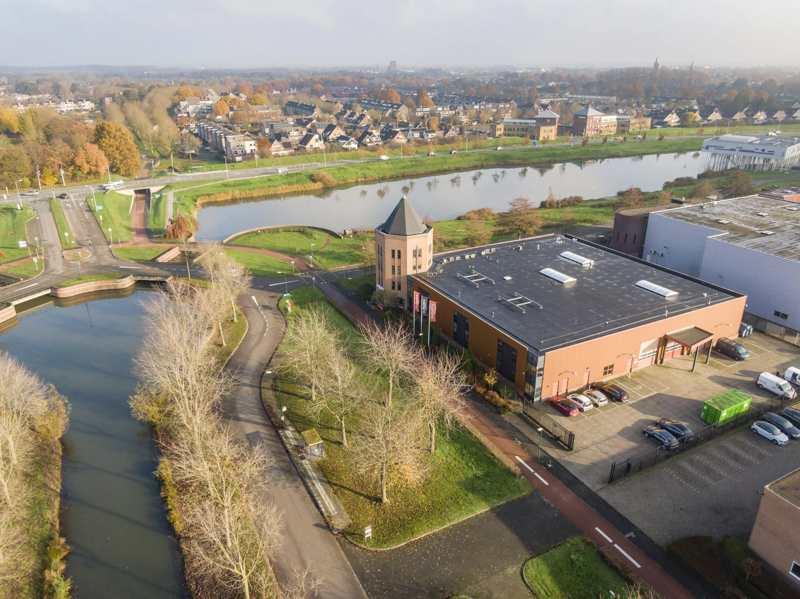 Luchtfoto van het kantoorgebouw aan Hoofdveste 2 in Houten, gelegen aan het water met parkeerplaatsen en omliggende infrastructuur.