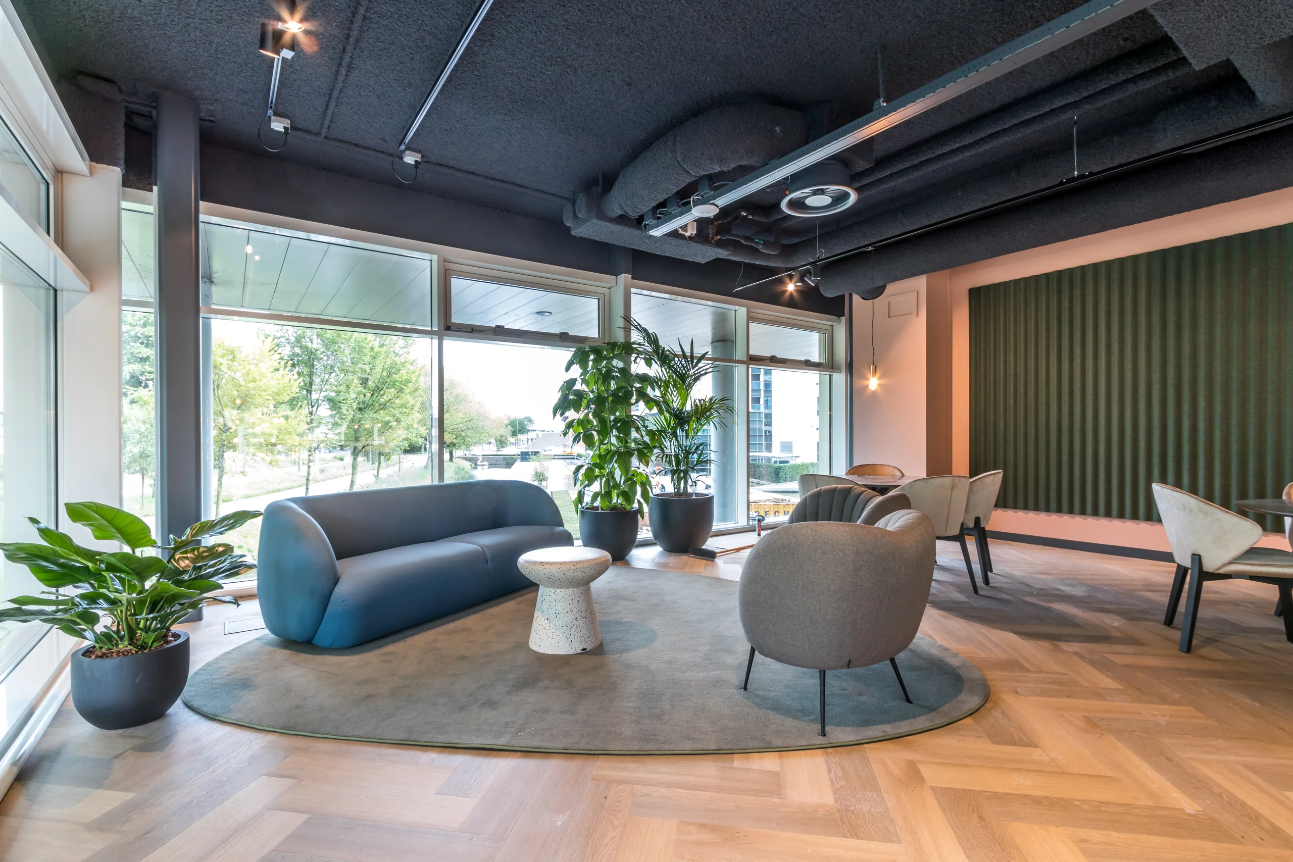 Moderne en licht ingerichte loungehoek in een kantoorruimte aan het John M. Keynesplein 10 in Amsterdam, met zithoek, planten en grote ramen.