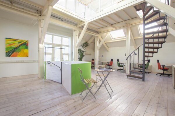 Een lichte en open kantoorruimte met bureaus, planten en een wenteltrap in Amsterdam.