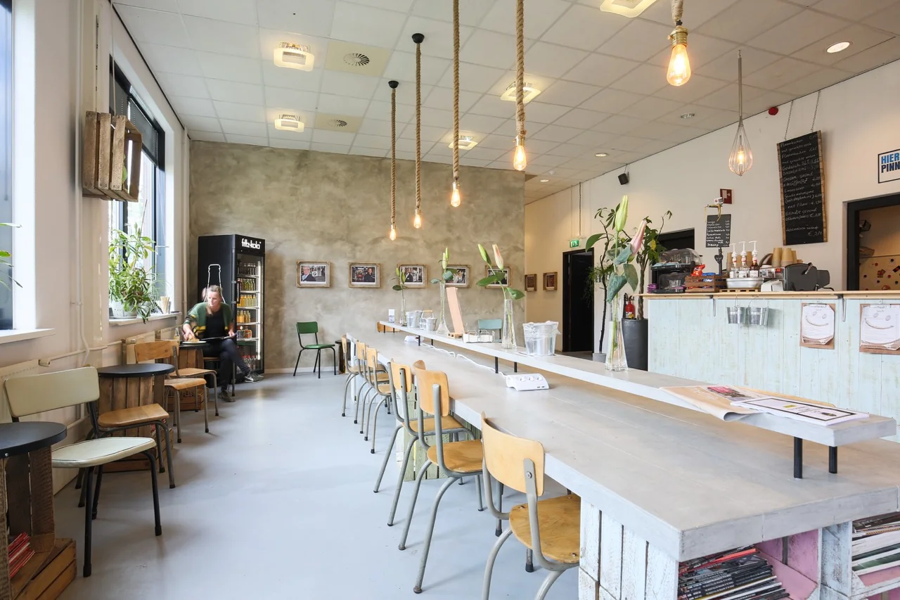 Moderne en lichte kantine met lange houten tafel, industriële accenten en planten aan de Lange Kleiweg 50-62 in Rijswijk.