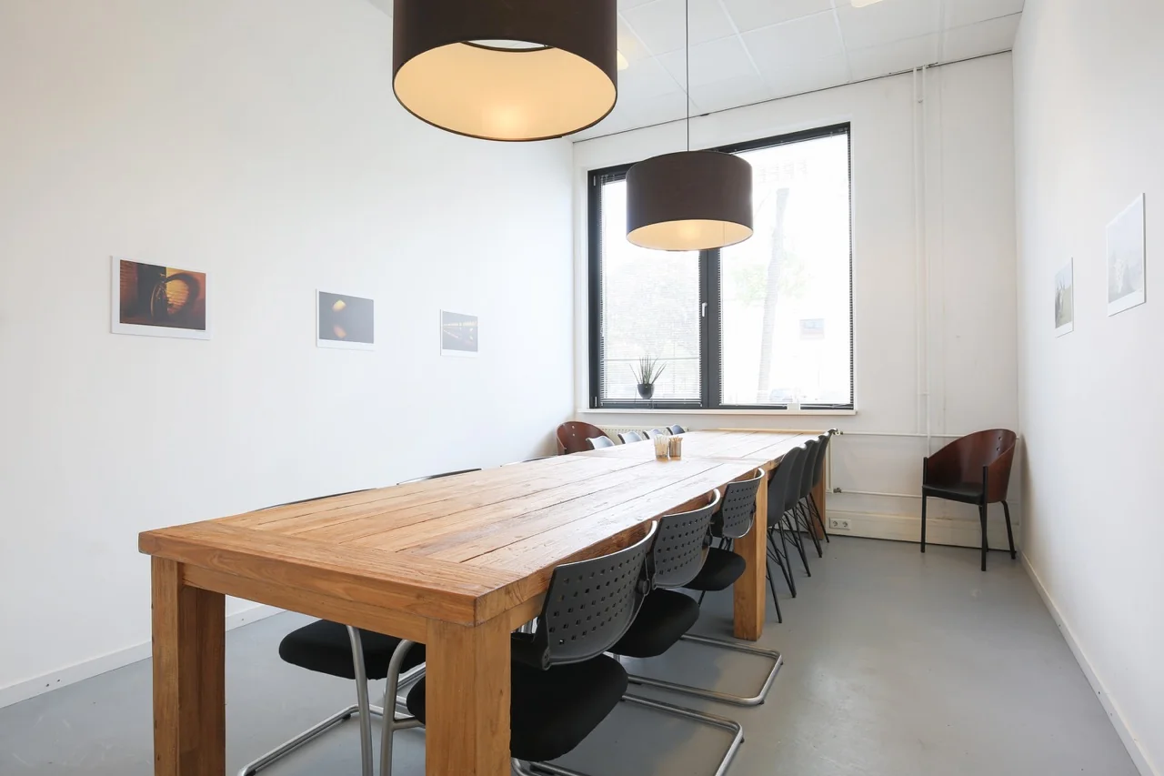 Vergaderruimte met lange houten tafel, zwarte stoelen en grote hanglampen in een kantoor aan de Lange Kleiweg 50-62 in Rijswijk.