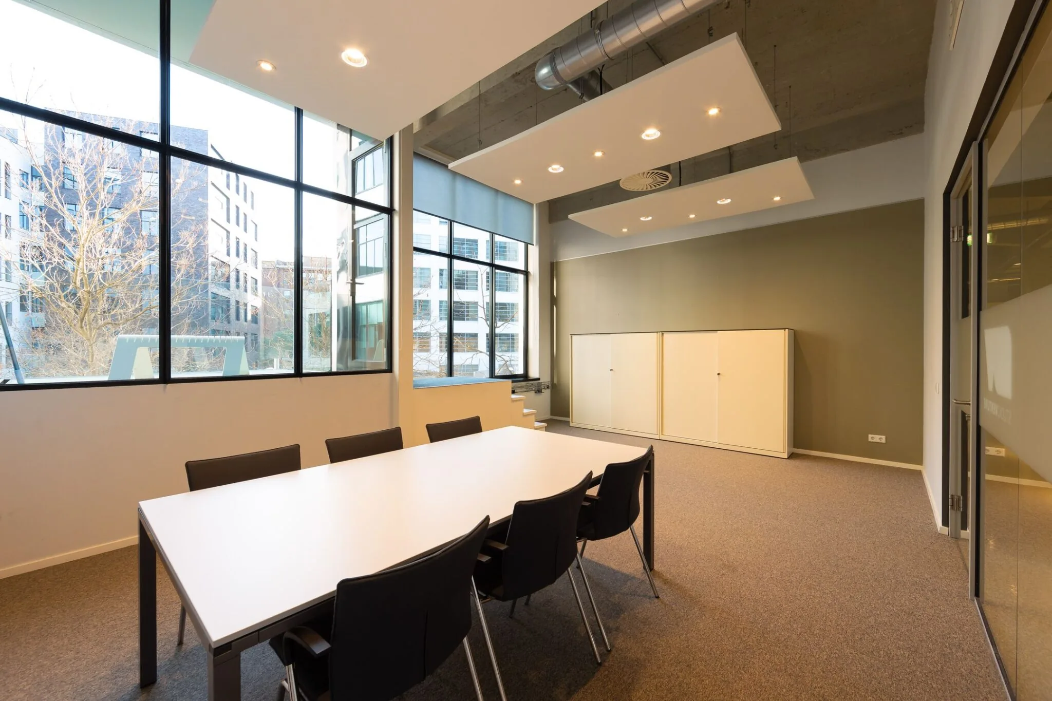 Moderne vergaderruimte in de Lichttoren 32 in Eindhoven met grote ramen, een witte tafel en zwarte stoelen.