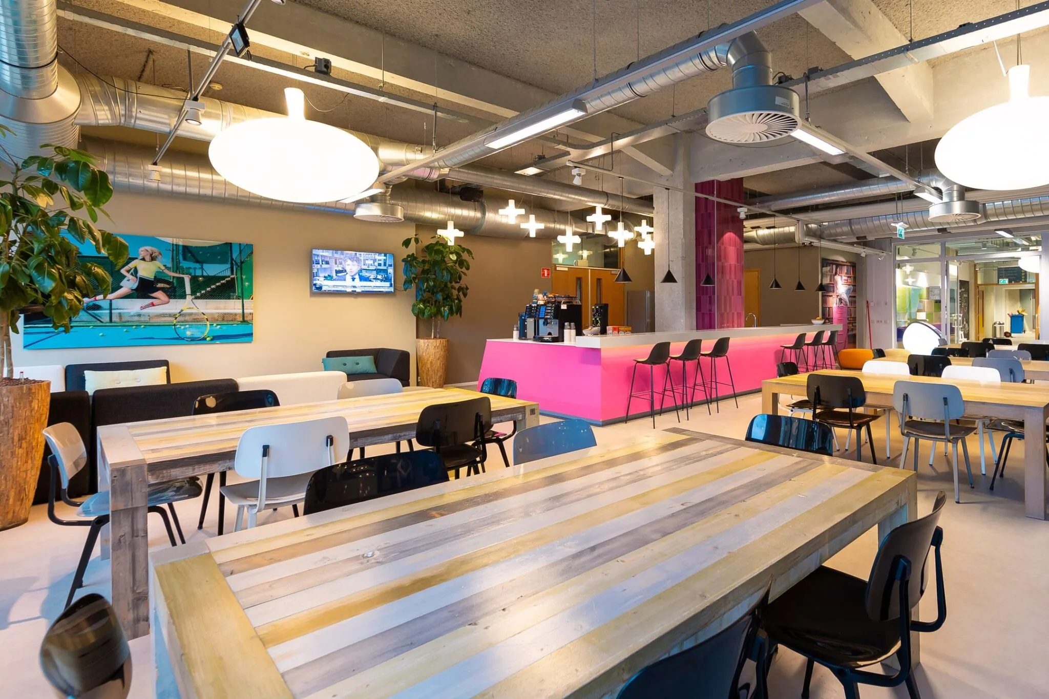 Moderne en kleurrijke kantoorruimte in de Lichttoren in Eindhoven met houten tafels, een felroze bar en industriële plafonddetails.