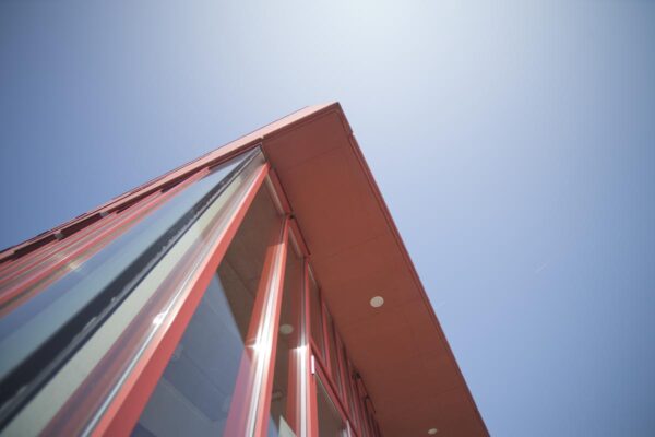 Schuin omhoog genomen close-up van de moderne glazen gevel met rode kozijnen van een kantoorruimte aan de Panamalaan in Amsterdam tegen een blauwe lucht.