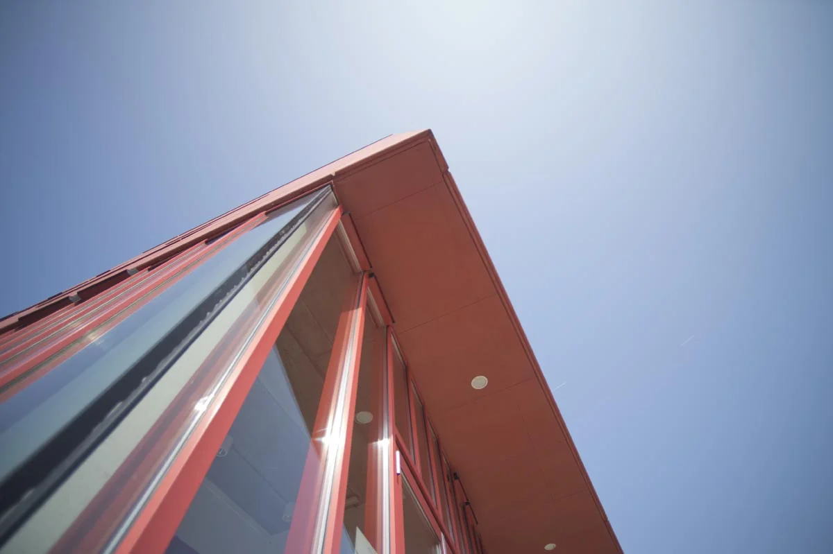 Schuin omhoog genomen close-up van de moderne glazen gevel met rode kozijnen van een kantoorruimte aan de Panamalaan in Amsterdam tegen een blauwe lucht.