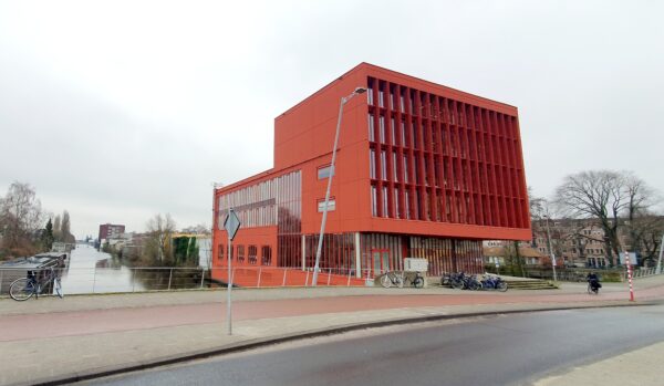 Modern rood kantoorgebouw aan de Panamalaan in Amsterdam, gelegen naast een waterkanaal.
