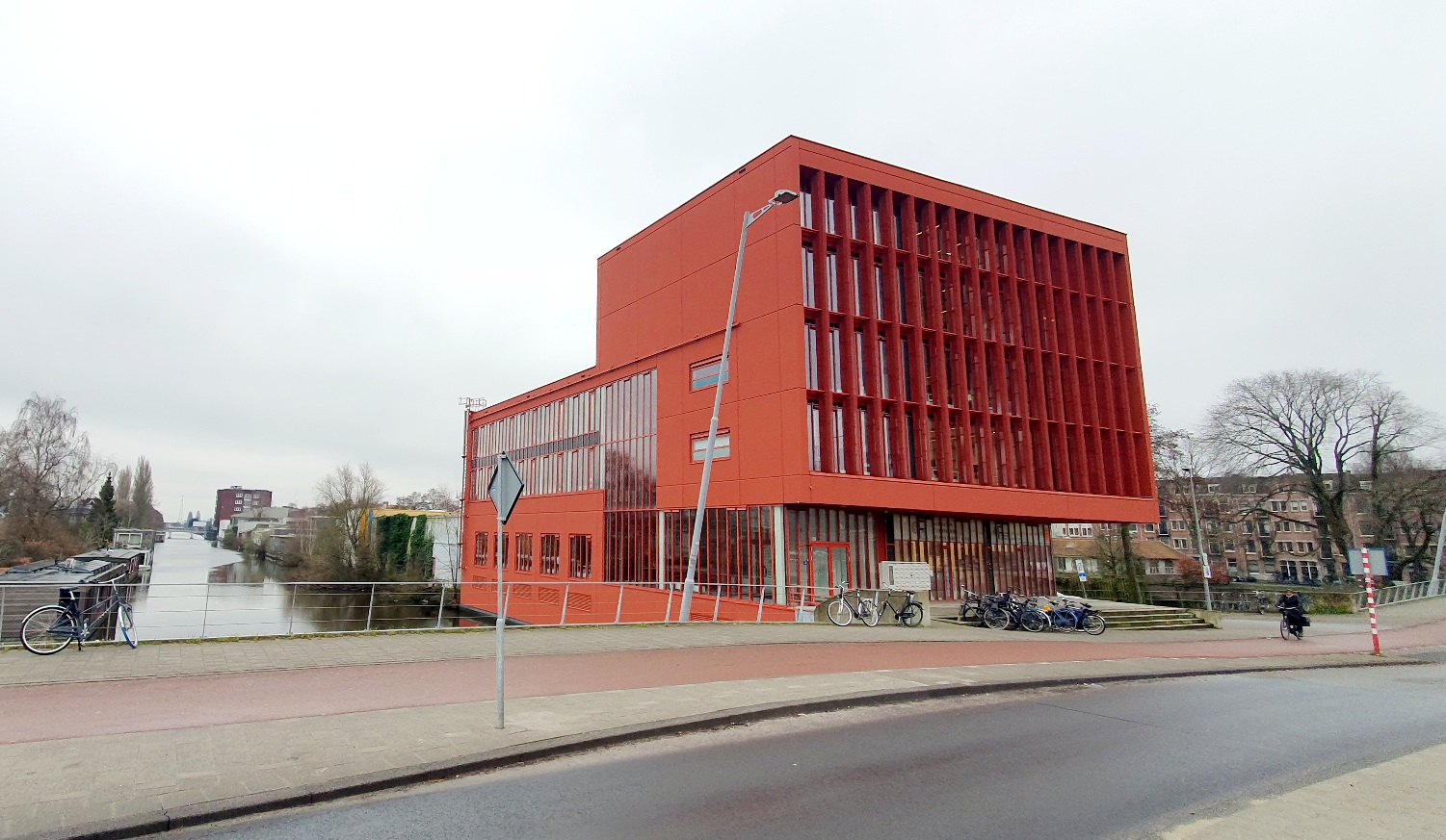 Modern rood kantoorgebouw aan de Panamalaan in Amsterdam, gelegen naast een waterkanaal.