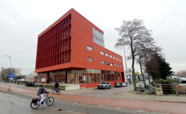 Modern rood kantoorgebouw aan de Panamalaan in Amsterdam met fietsers en geparkeerde auto's op de voorgrond.