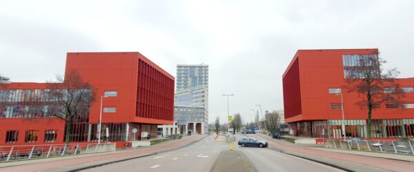Twee felrode kantoorgebouwen aan de Panamalaan in Amsterdam met een modern hoogbouwpand op de achtergrond.