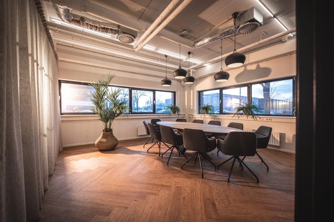 Moderne vergaderruimte met ovale tafel, zwarte stoelen, houten vloer en grote ramen in kantoor aan de Rietbaan 2-12 in Capelle aan den IJssel.