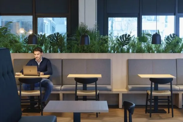 Moderne kantoorruimte aan de Rietbaan 2-12 in Capelle aan den IJssel met zitgedeelte, plantenwand en werkende man op laptop.