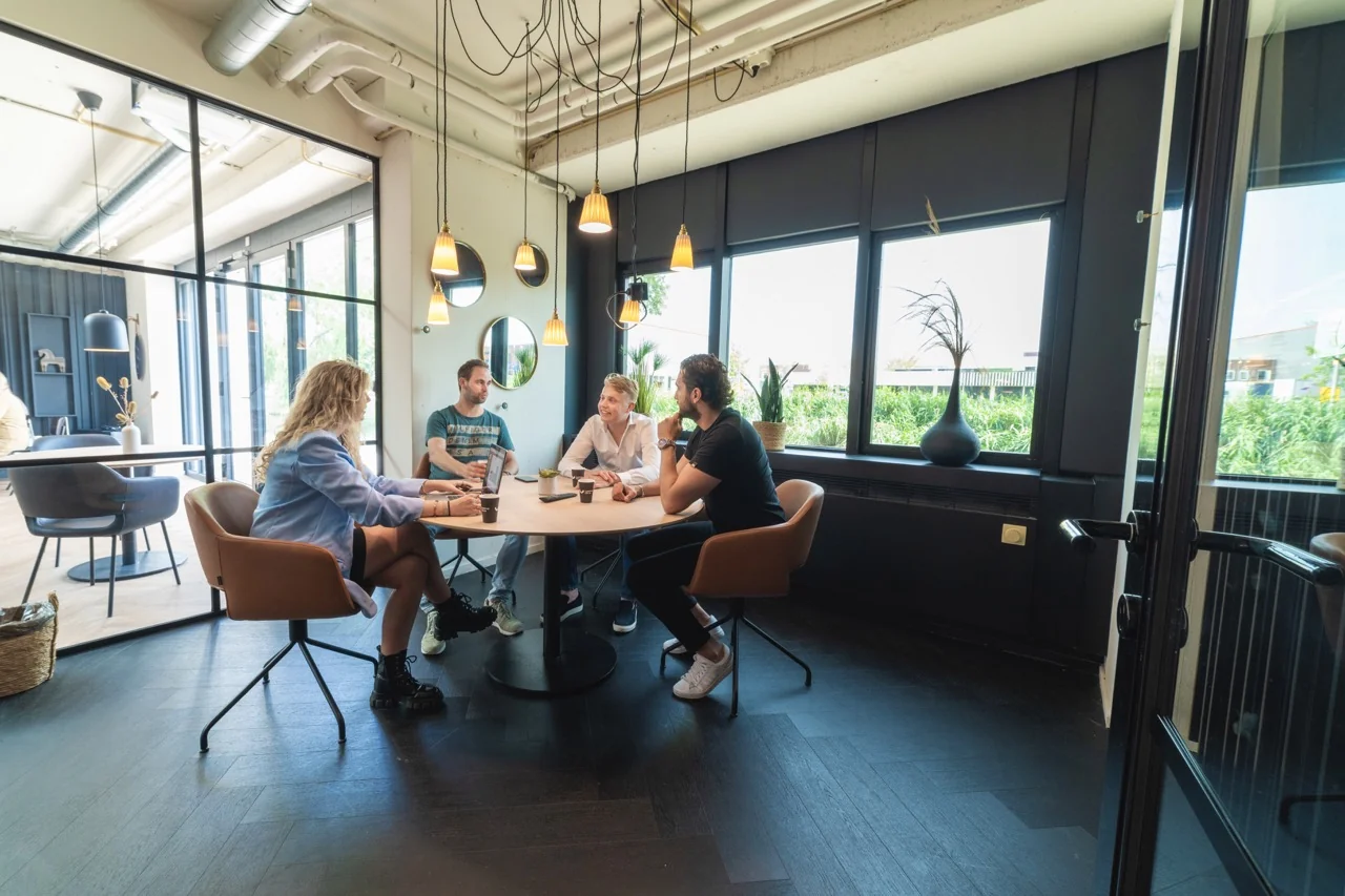 Vier mensen overleggen aan een ronde tafel in een moderne kantoorruimte aan de Rietbaan 2-12 in Capelle aan den IJssel.