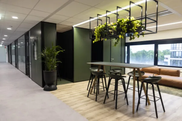 Modern office space at Rijnzathe 6 in De Meern with a high table, bar stools, hanging plants, and a lounge area.