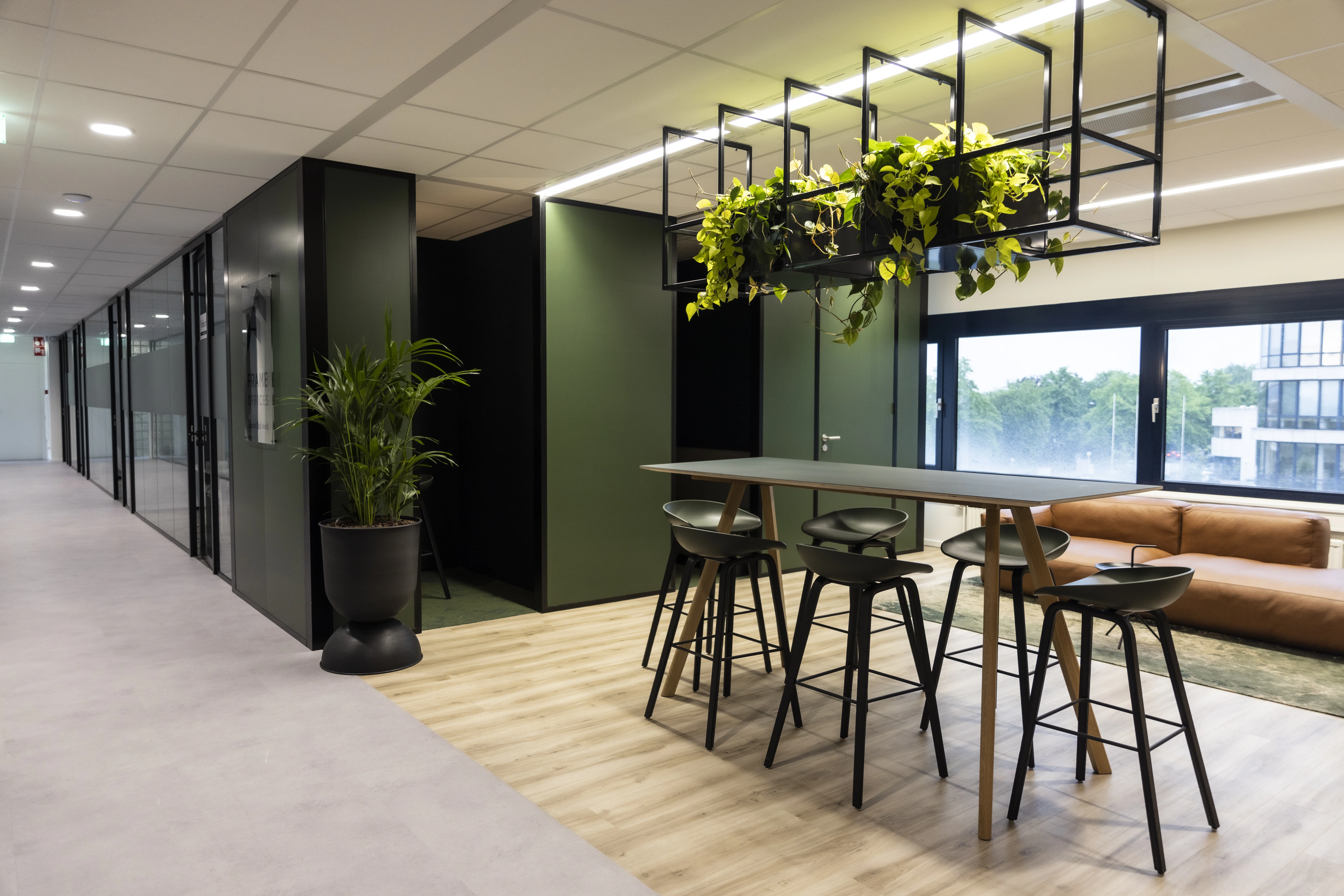 Modern office space at Rijnzathe 6 in De Meern with a high table, bar stools, hanging plants, and a lounge area.