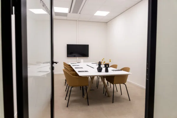 Modern meeting room at Rijnzathe 6 in De Meern with a long table, mustard-colored chairs, and a wall-mounted screen.