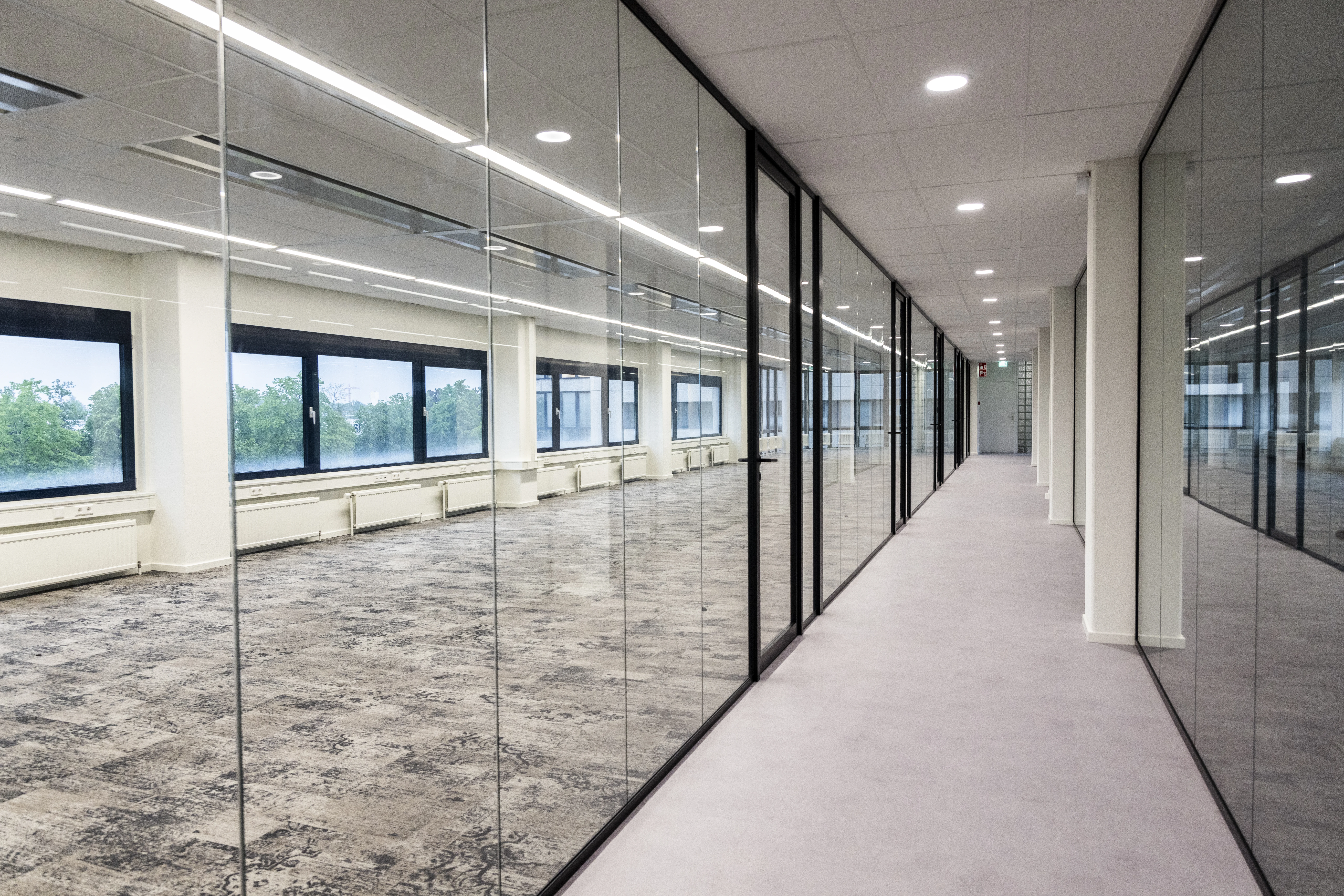 Modern office space for rent at Rijnzathe 6 in De Meern, featuring glass walls and large windows along a bright corridor.