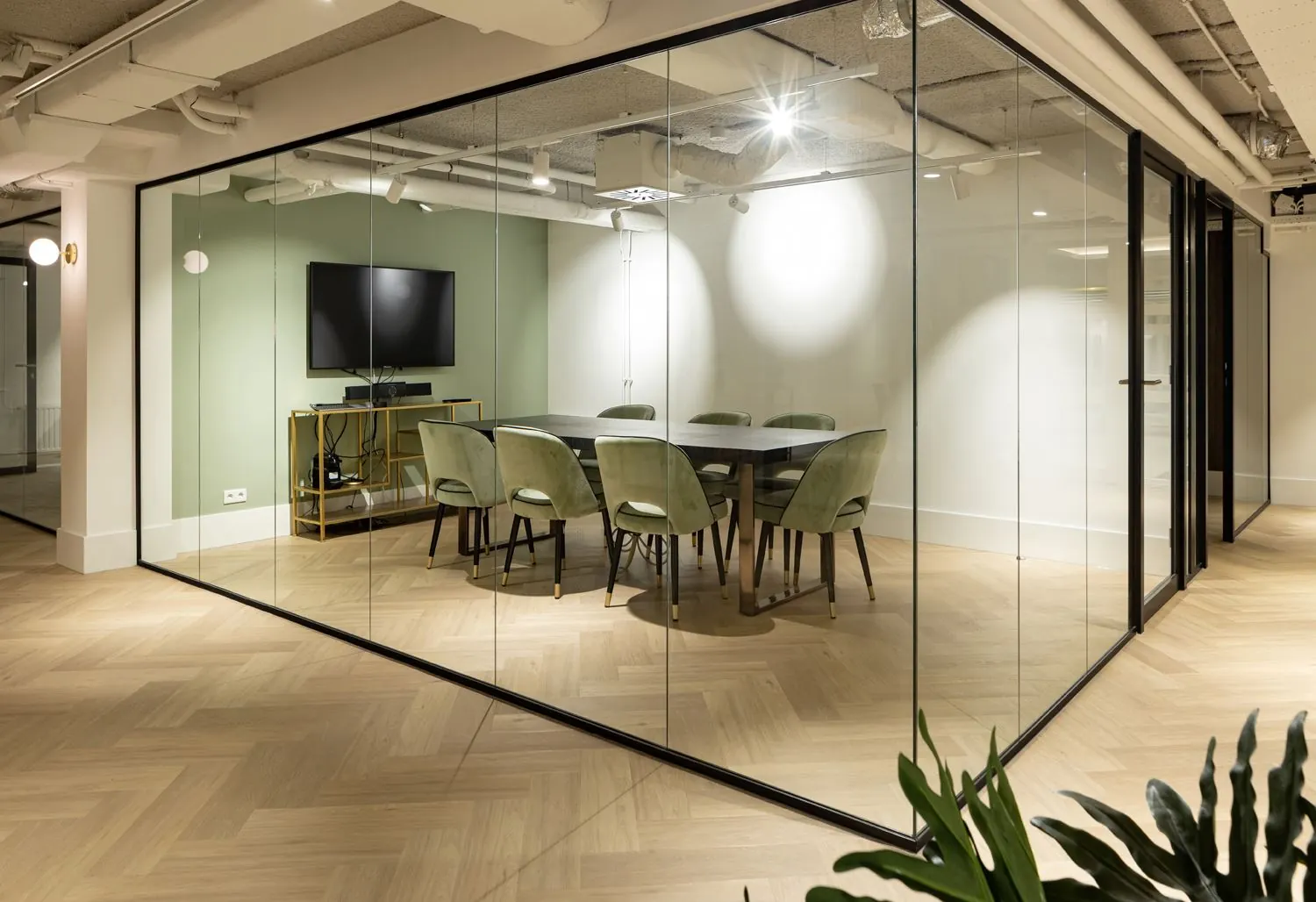 Moderne vergaderruimte met glazen wanden, een grote tafel, groene stoelen en een tv in kantoorruimte aan de Siriusdreef 60 in Hoofddorp.