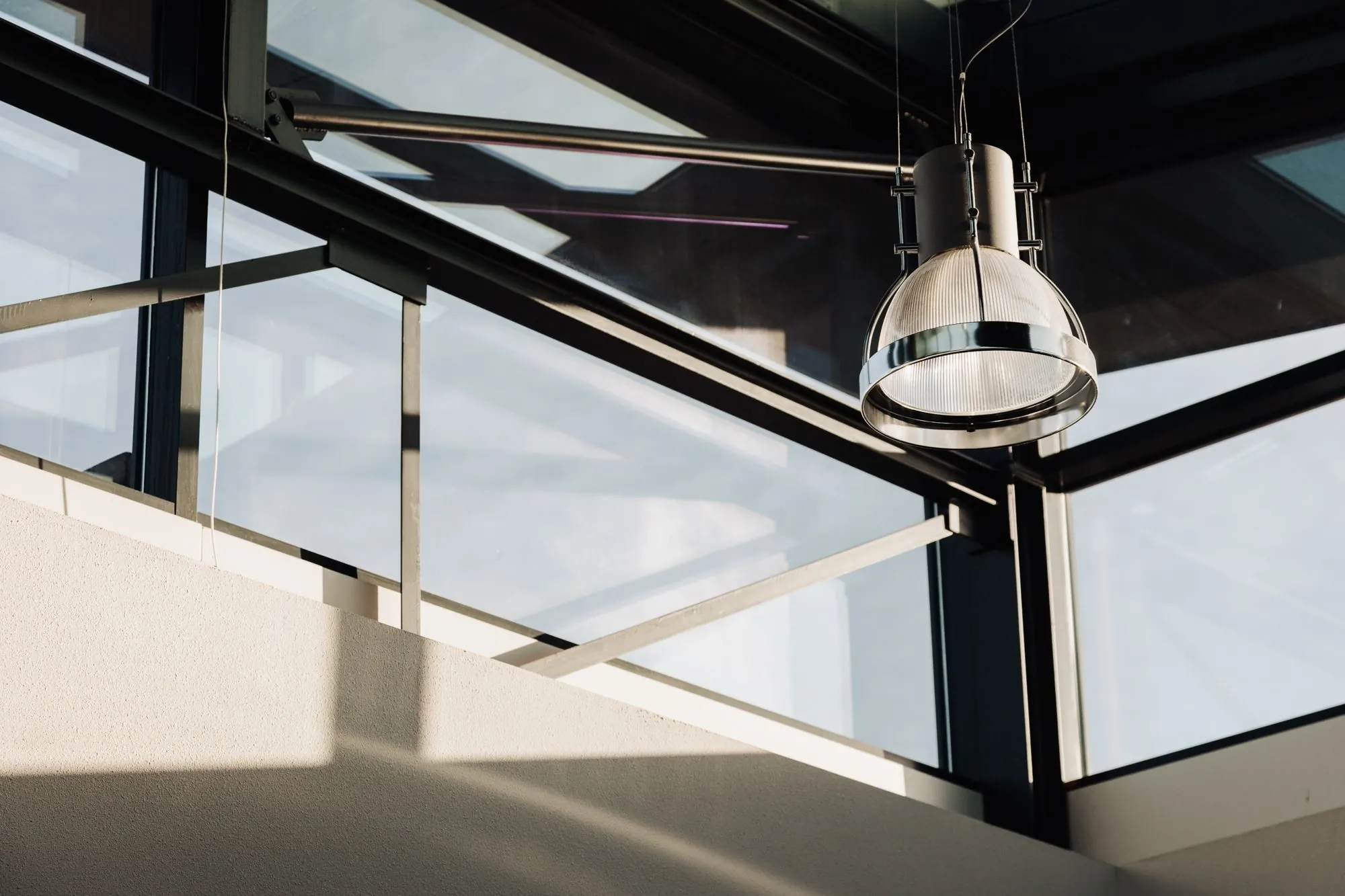 Moderne industriële hanglamp bij een glazen gevel in kantoorruimte aan de Sloterweg 303 in Badhoevedorp.