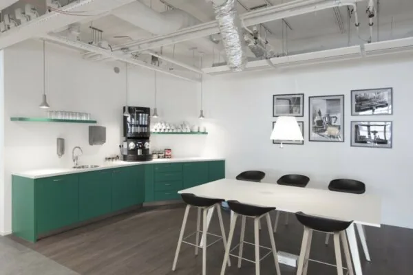 Moderne koffie- en lunchruimte in een kantoor aan de St. Jacobsstraat 123-135 in Utrecht, met groene keukenkasten, een koffiemachine en een witte vergadertafel met barkrukken.