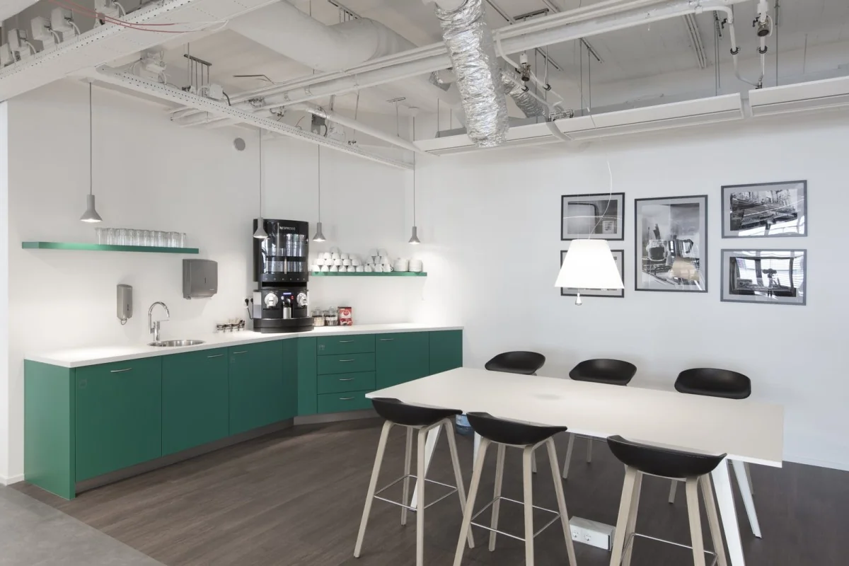 Moderne koffie- en lunchruimte in een kantoor aan de St. Jacobsstraat 123-135 in Utrecht, met groene keukenkasten, een koffiemachine en een witte vergadertafel met barkrukken.