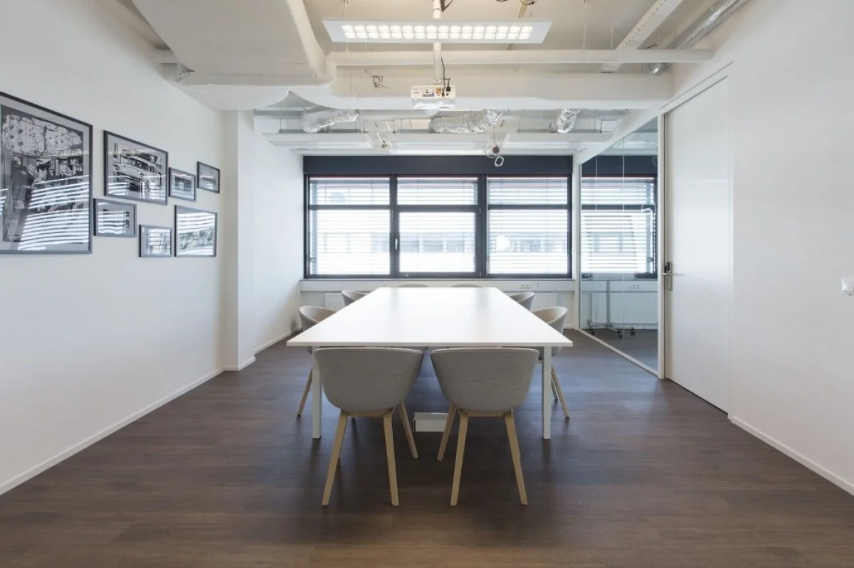 Moderne vergaderruimte met een lange witte tafel, grijze stoelen en grote ramen in een kantoor aan de St. Jacobsstraat 123-135 in Utrecht.
