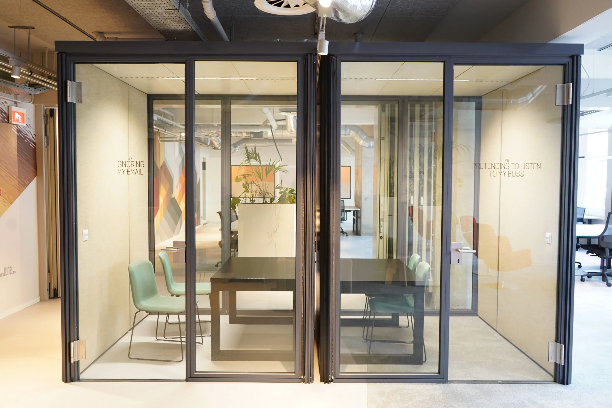 Twee glazen vergaderruimtes in een modern kantoor aan het Weesperplein 4A in Amsterdam, ingericht met stoelen en tafels.