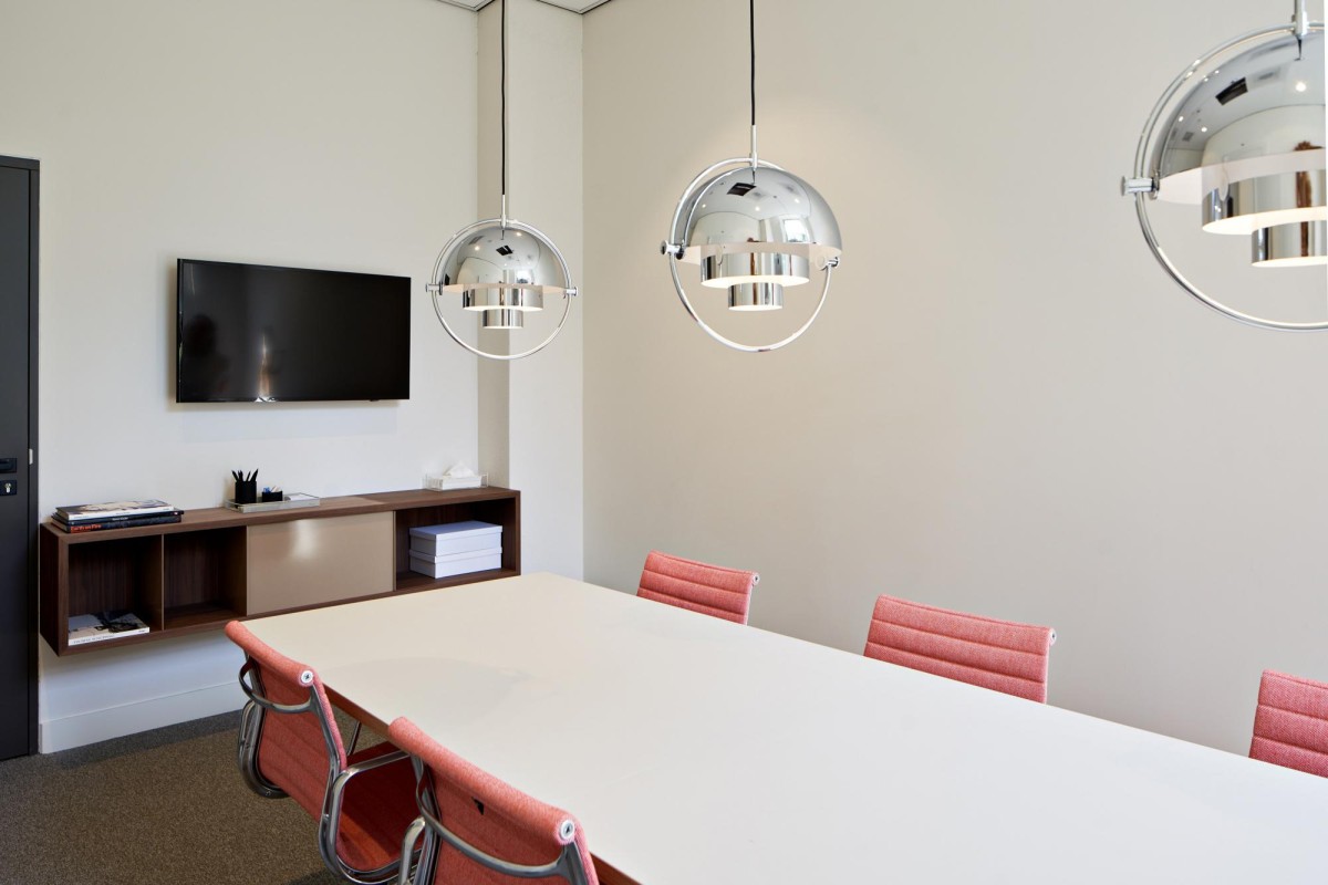 Vergaderruimte op Keizersgracht 555 in Amsterdam met moderne hanglampen, rode stoelen en een flatscreen tv.