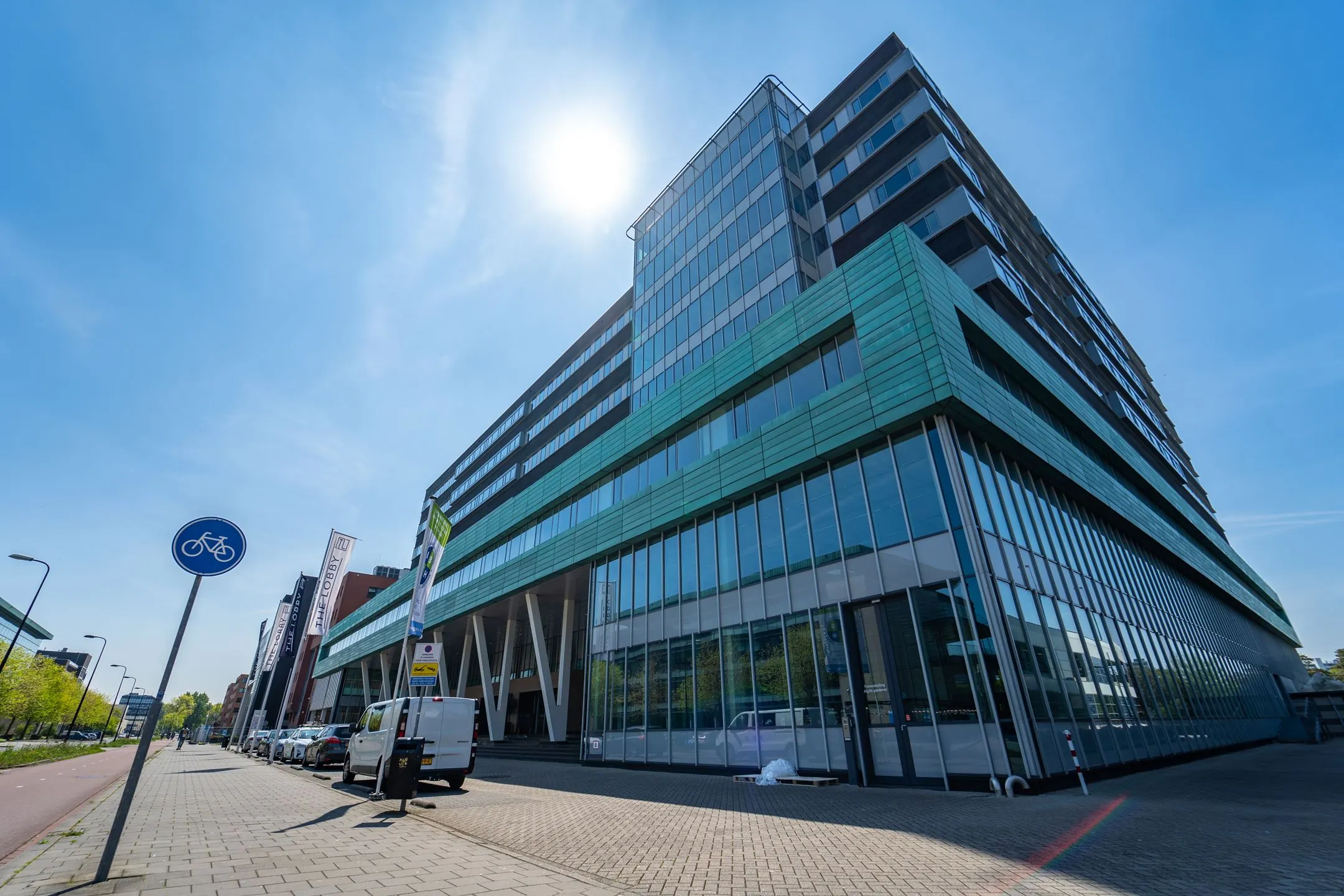 Modern kantoorgebouw aan de Lange Kleiweg 6-28 met glazen gevel en groene accenten, gezien vanaf de straat op een zonnige dag.