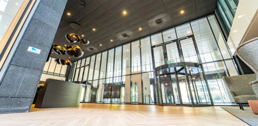 Moderne entreehal van een kantoorpand aan de Lange Kleiweg met glazen wanden, houten vloer, en een draaideur.