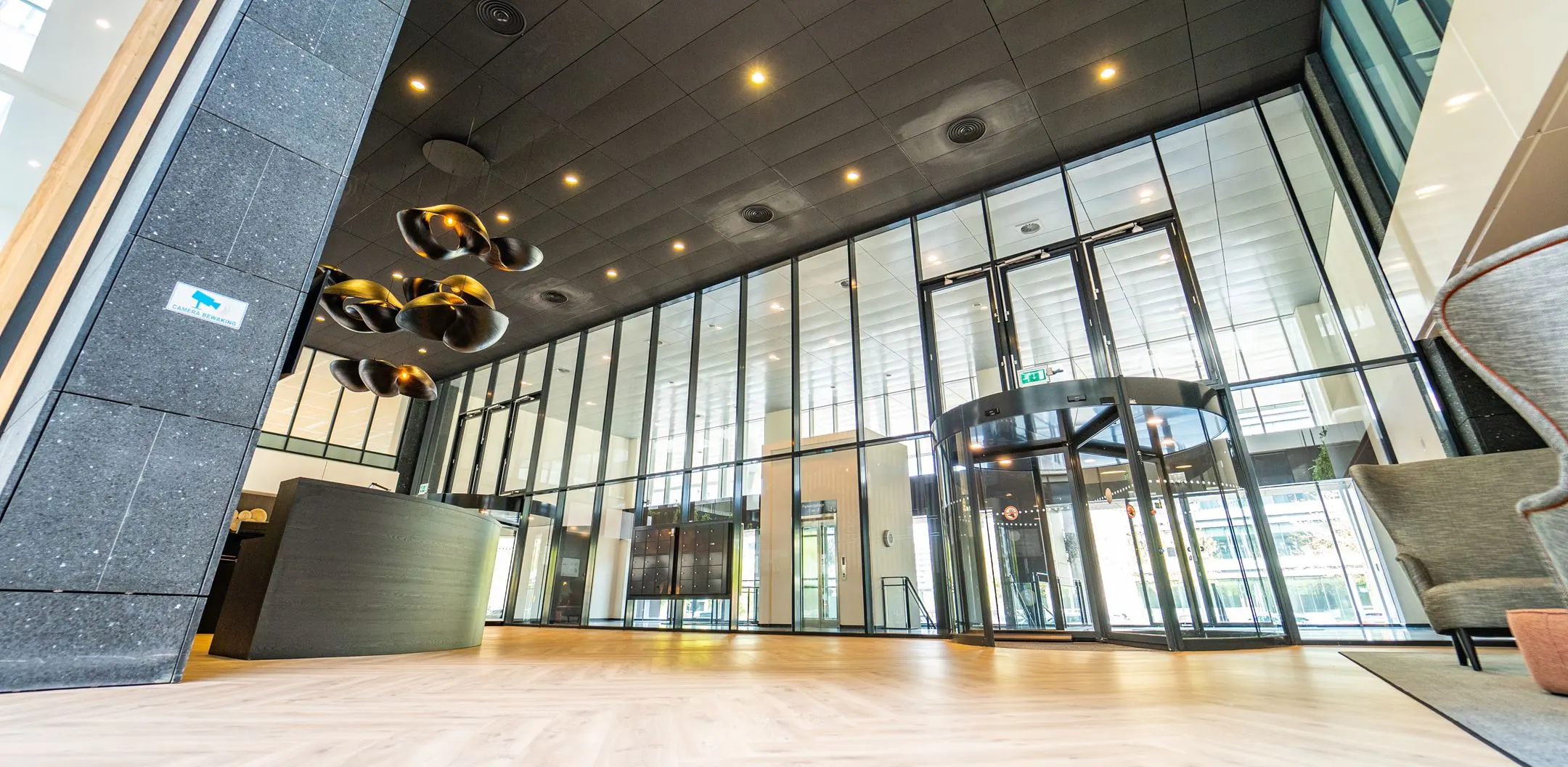 Moderne entreehal van een kantoorpand aan de Lange Kleiweg met glazen wanden, houten vloer, en een draaideur.