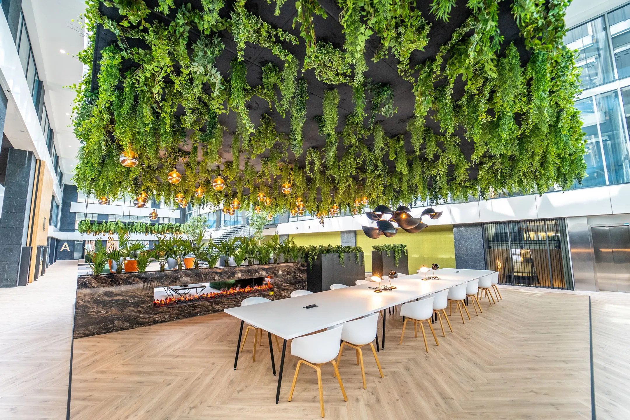 Moderne kantoorruimte aan de Lange Kleiweg met groene plafonddecoratie, lange werktafels en een stijlvolle open haard.