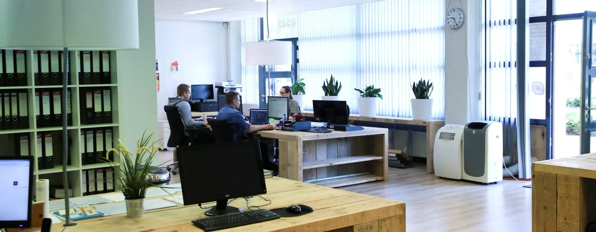 Moderne kantoorruimte aan de Kanaaldijk-Zuid 19 met houten bureaus, werkende medewerkers en veel daglicht.