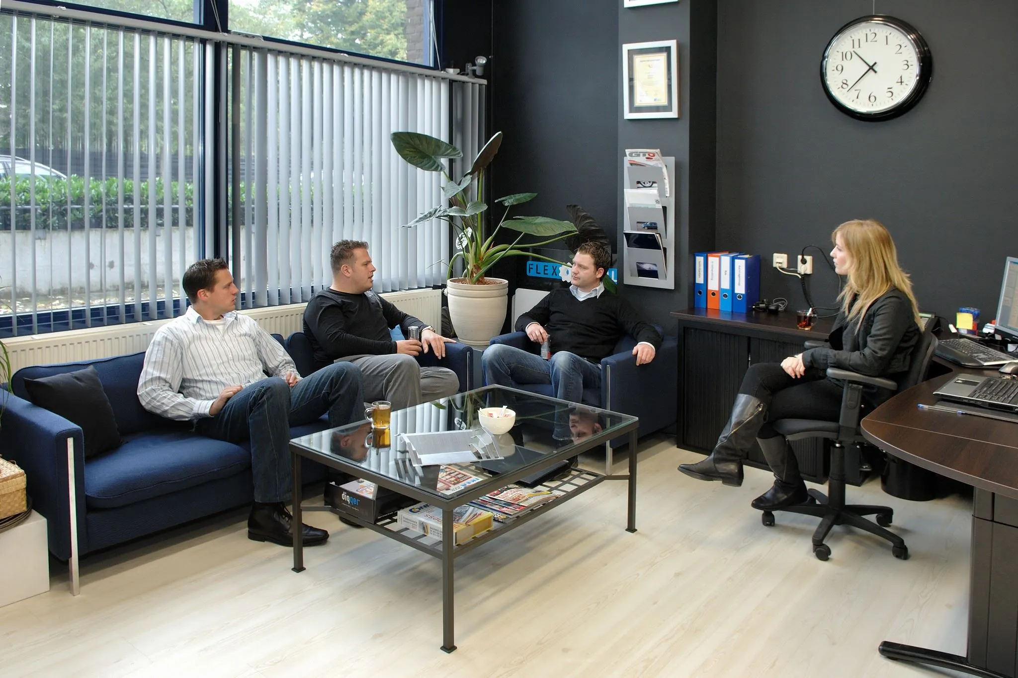 Vier mensen zitten in een moderne kantoorruimte aan de Kanaaldijk-Zuid 19 in gesprek met een vrouw achter een bureau.