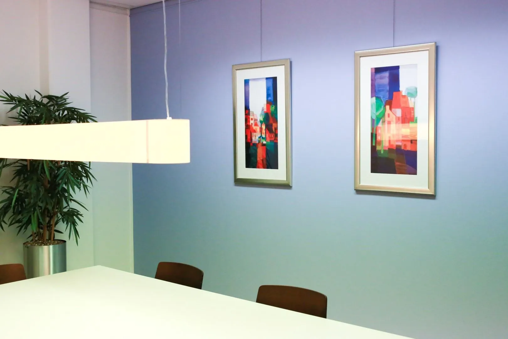 Vergaderruimte in kantoor aan Kanaaldijk-Zuid 19 met moderne kunst aan de muur en een hanglamp boven een witte tafel.