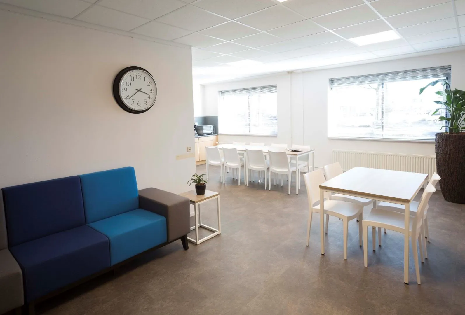 Moderne en lichte kantoorruimte aan de Steenovenweg 5 met zitgedeelte, eettafels en grote ramen.