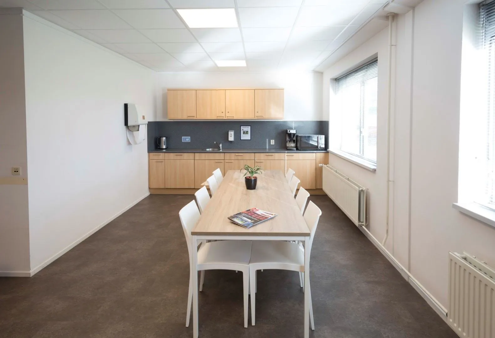 Moderne pantry met lange tafel en acht stoelen in kantoorruimte aan de Steenovenweg 5.