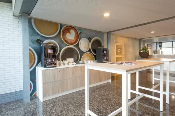 Moderne koffiecorner in een kantoorruimte aan de Steenovenweg 5, met koffiemachines, houten kasten en een wanddecoratie van koffiekopjes.